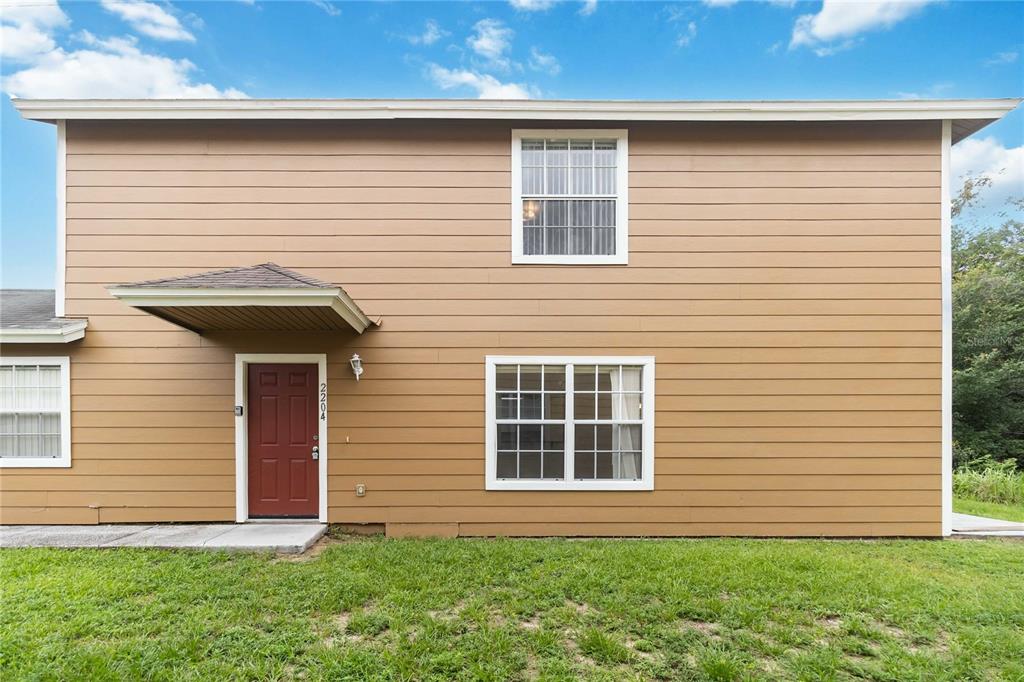 A two-story house exterior features tan horizontal siding, a red front door, and white-trimmed windows — 2204 FAN PALM DRIVE, DAVENPORT, FL