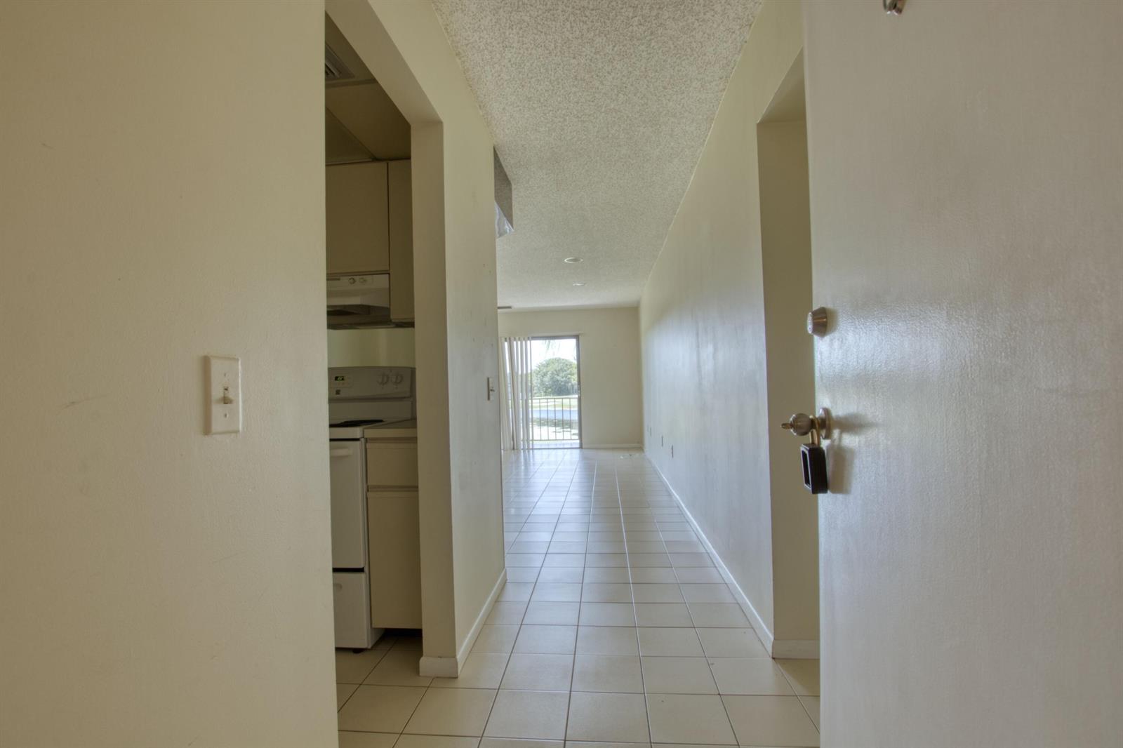 A view from an entryway looking down a tiled hallway toward a kitchen and balcony — 4657 Fountains Drive S # 206, FL 33467, FL