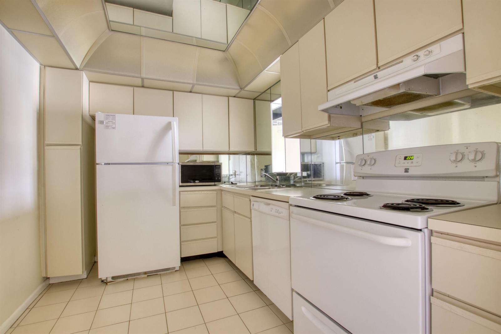 A kitchen features white appliances, light-colored cabinetry, tiled flooring, and a mirrored backsplash — 4657 Fountains Drive S # 206, FL 33467, FL