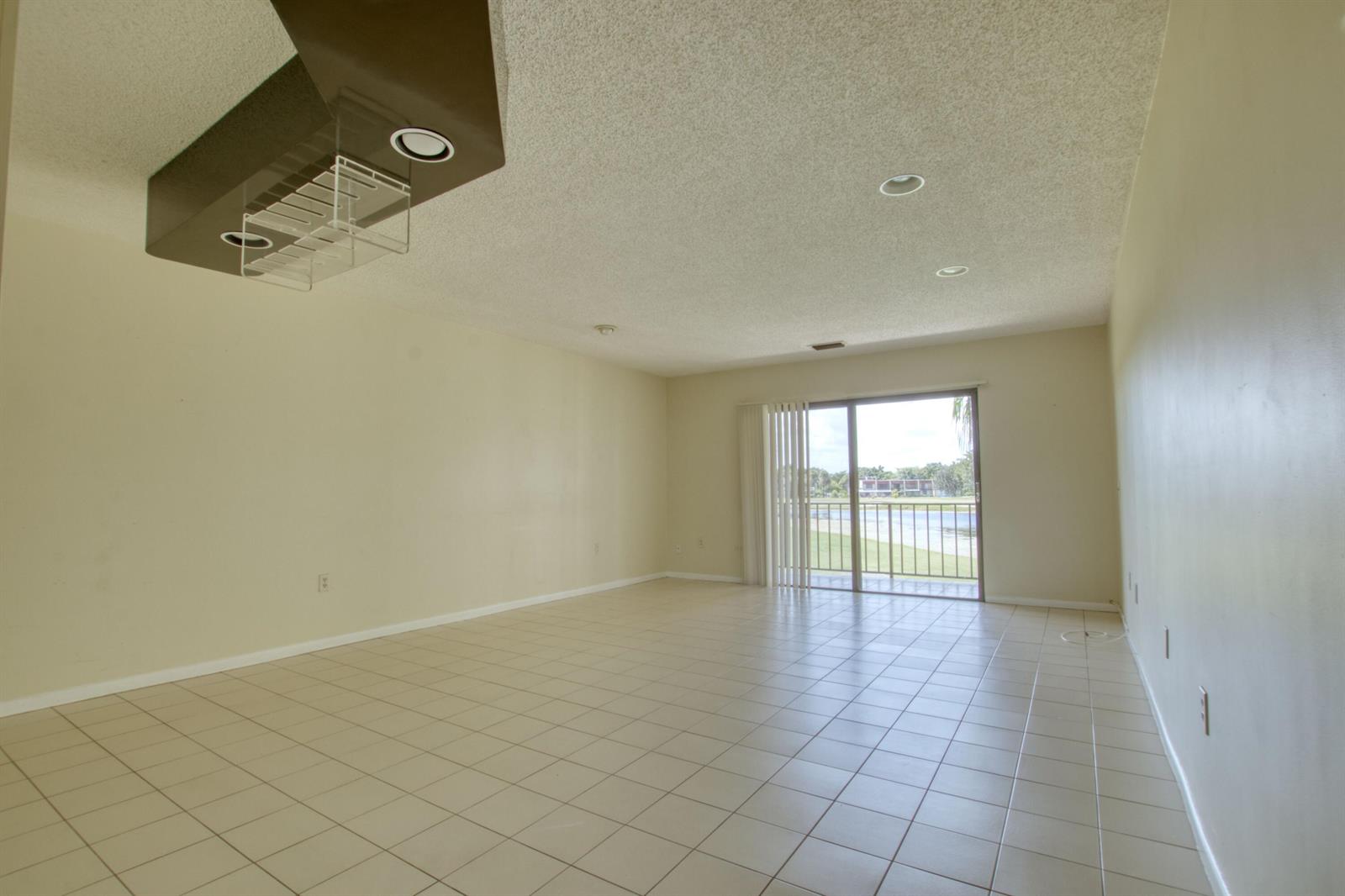 An empty living room features beige tile flooring, a textured ceiling, and a sliding glass door — 4657 Fountains Drive S # 206, FL 33467, FL