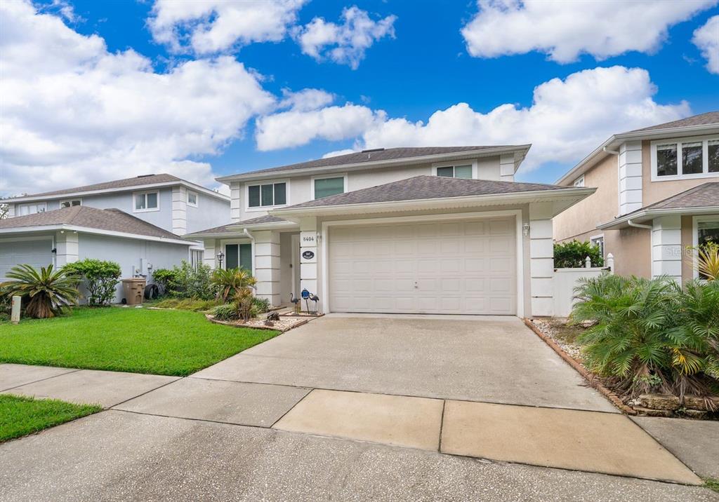 A two-story suburban house with a beige exterior, a two-car garage, and a concrete driveway — 8404 RISING STAR COURT, KISSIMMEE, FL