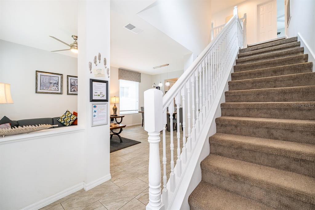 A carpeted staircase with a white railing leads to an upper level near a living area — 8404 RISING STAR COURT, KISSIMMEE, FL
