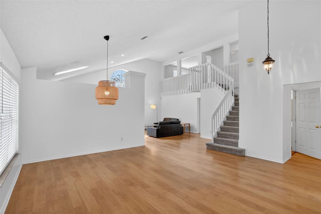 A bright living room features hardwood floors, a vaulted ceiling, and a staircase with railings — 2809 RUNYON CIRCLE, ORLANDO, FL