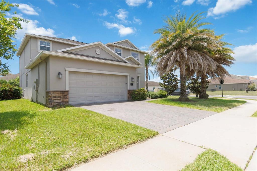 A two-story suburban house features a beige stucco exterior, stone accents, and a paved driveway — 472 BRUNSWICK DRIVE, DAVENPORT, FL