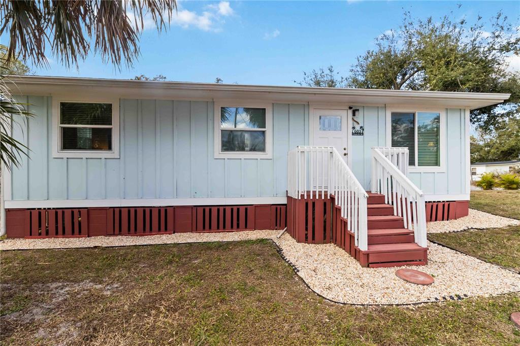 A light blue house with vertical siding, a red foundation skirt, and a wooden staircase — 603 CHURCH STREET, NOKOMIS, FL