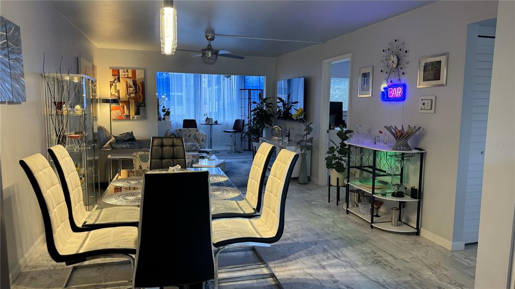 A dining area with a glass table and white chairs sits adjacent to a bar cart — 1243 S MARTIN LUTHER KING JR AVENUE UNIT B205, CLEARWATER, FL
