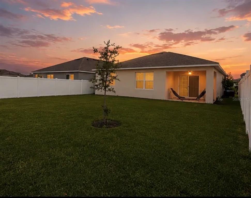 A backyard view of a house with a covered patio and a white vinyl fence — 1782 HIDEOUT STREET, KISSIMMEE, FL