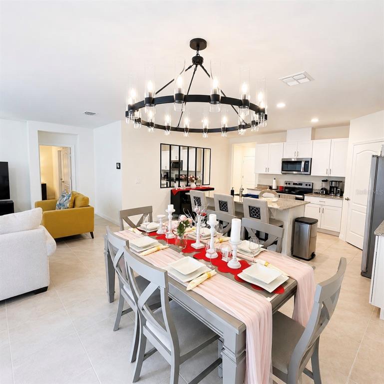 A dining area with a large circular chandelier, gray table and chairs, and an open kitchen — 1782 HIDEOUT STREET, KISSIMMEE, FL