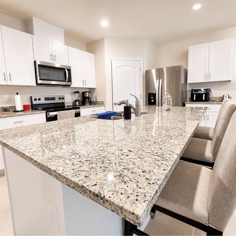 A kitchen features white cabinets, granite countertops, a large island with seating, and stainless steel appliances — 1782 HIDEOUT STREET, KISSIMMEE, FL