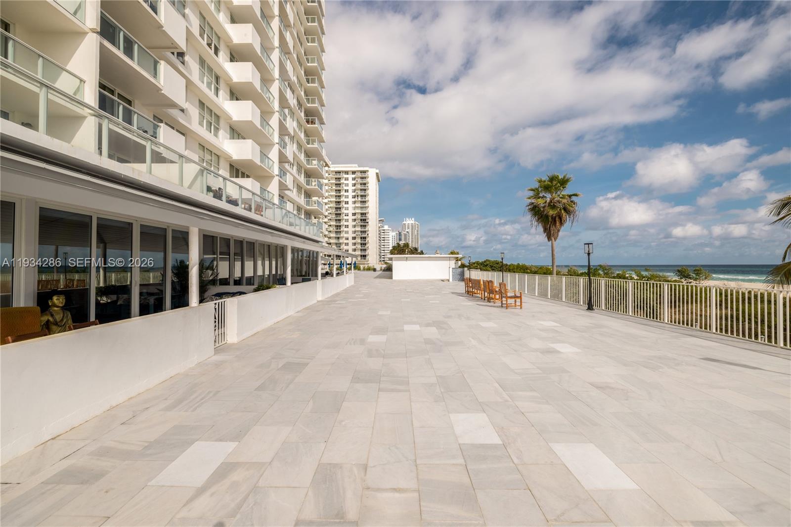 A large, paved outdoor terrace overlooks the ocean with a tall residential building nearby — 5601 Collins Ave # 1019, Miami Beach FL 33140, MIAMI BEACH, FL