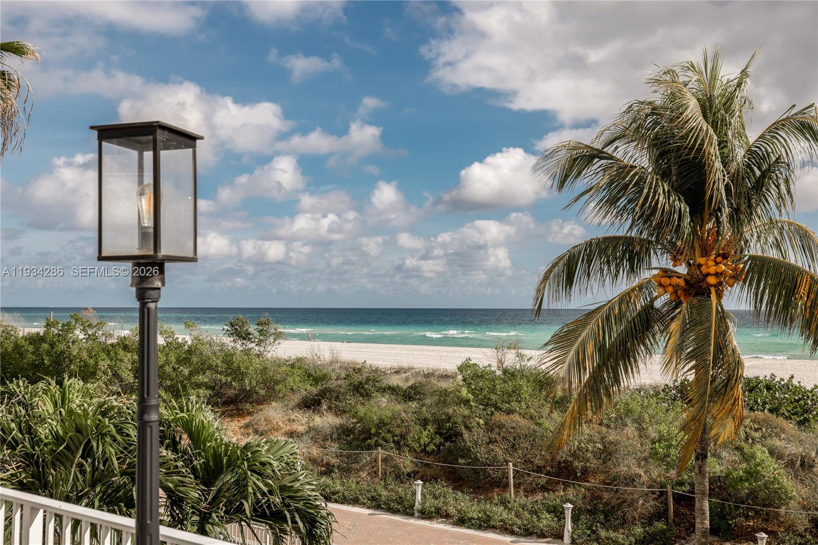 A view of a beach and ocean from a balcony with a lamp and palm tree — 5601 Collins Ave # 1019, Miami Beach FL 33140, MIAMI BEACH, FL