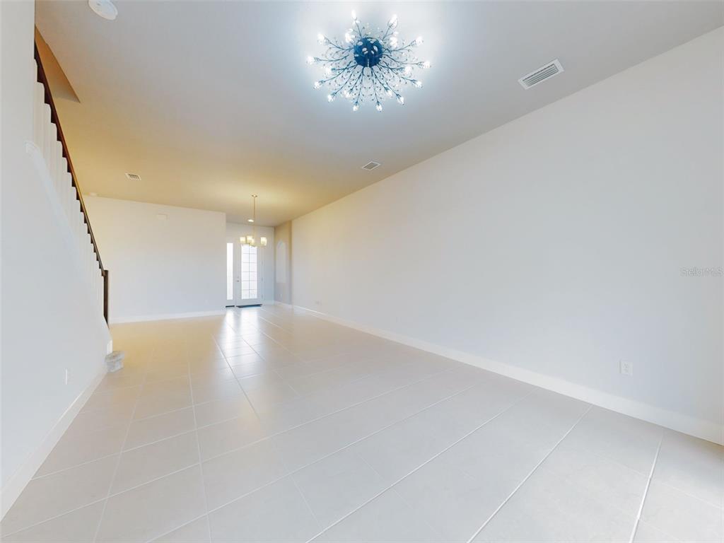 An empty room with light tile floors, white walls, a staircase, and two light fixtures — 6321 HANFIELD DRIVE, PORT ORANGE, FL