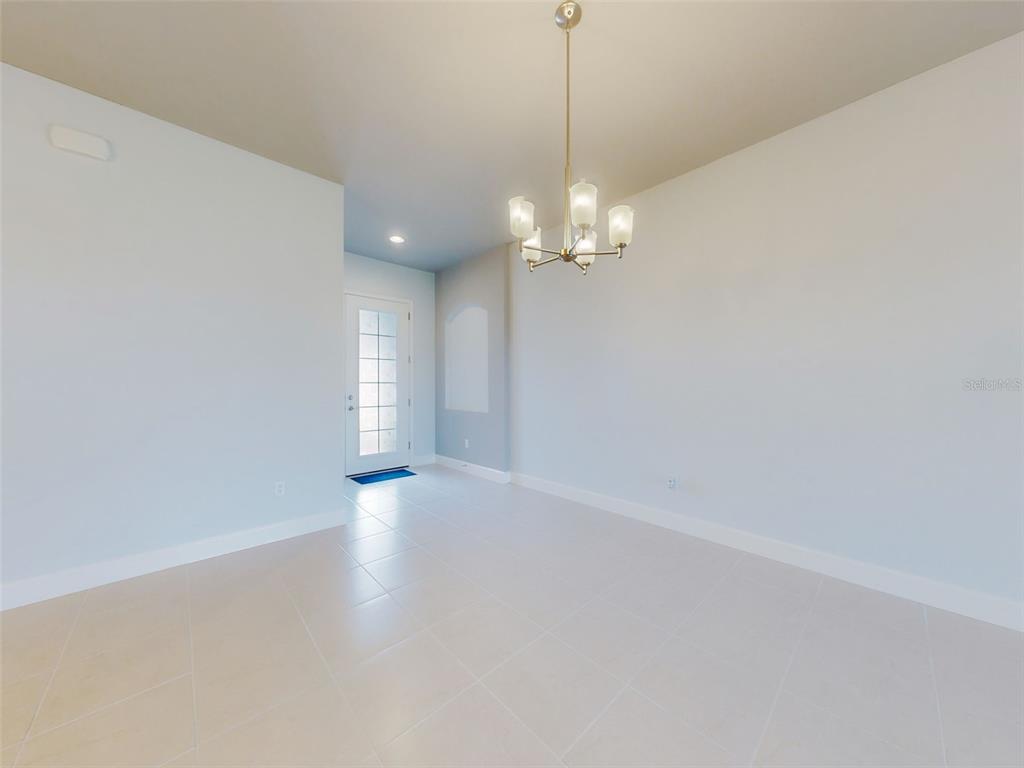 An empty dining room features light tile flooring, a chandelier, and a front entry door — 6321 HANFIELD DRIVE, PORT ORANGE, FL