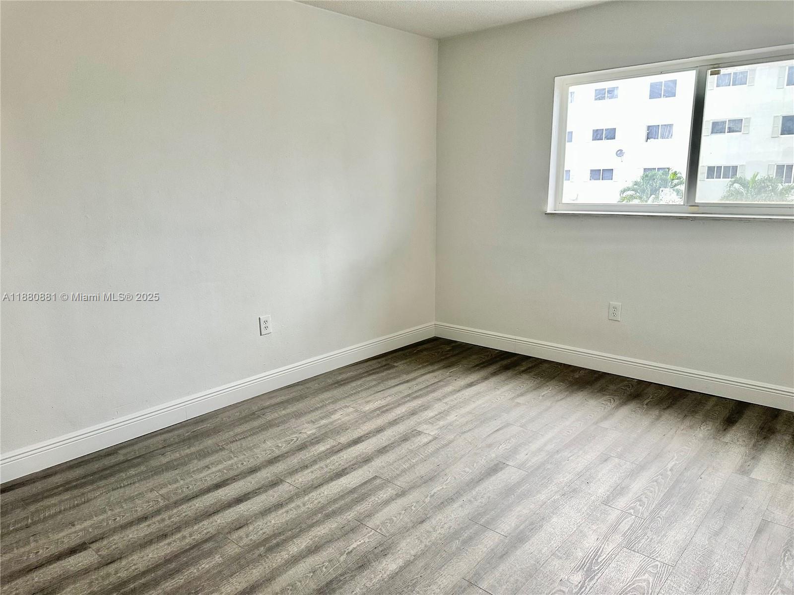 An empty room features light gray walls, white baseboards, and wood-look laminate flooring — 13285 NE 6th Ave # 301, North Miami FL 33161, NORTH MIAMI, FL