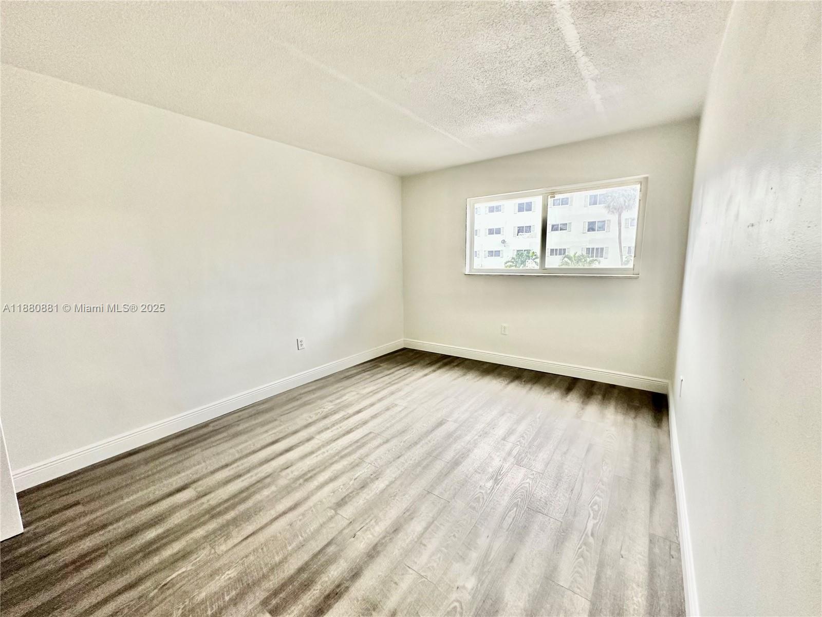 An empty bedroom features light gray wood-look flooring, white walls, and a single window — 13285 NE 6th Ave # 301, North Miami FL 33161, NORTH MIAMI, FL