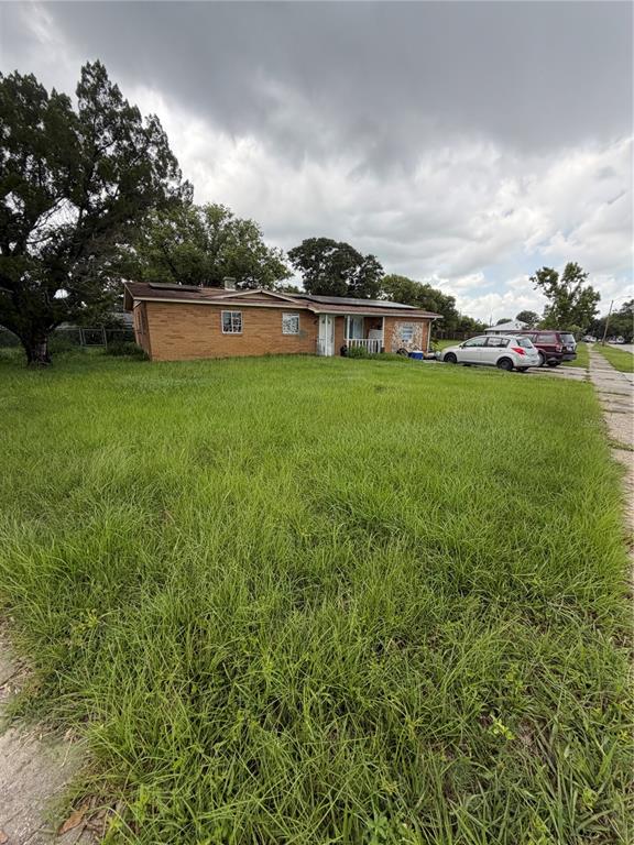 A single-story brick house with a large, overgrown front lawn under a cloudy sky — 2880 SATURN DRIVE, TITUSVILLE, FL