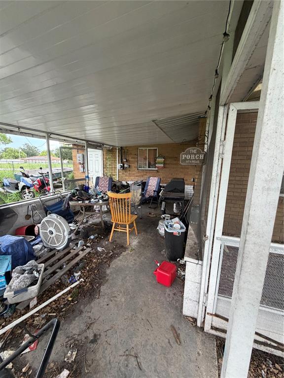 A cluttered covered porch features a yellow wooden chair, outdoor furniture, and a metal sign — 2880 SATURN DRIVE, TITUSVILLE, FL