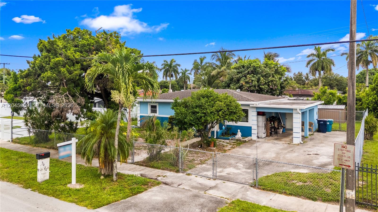 A single-story blue house with a carport sits behind a chain-link fence — 3030 NW 176th St, Miami Gardens FL 33056, MIAMI GARDENS, FL