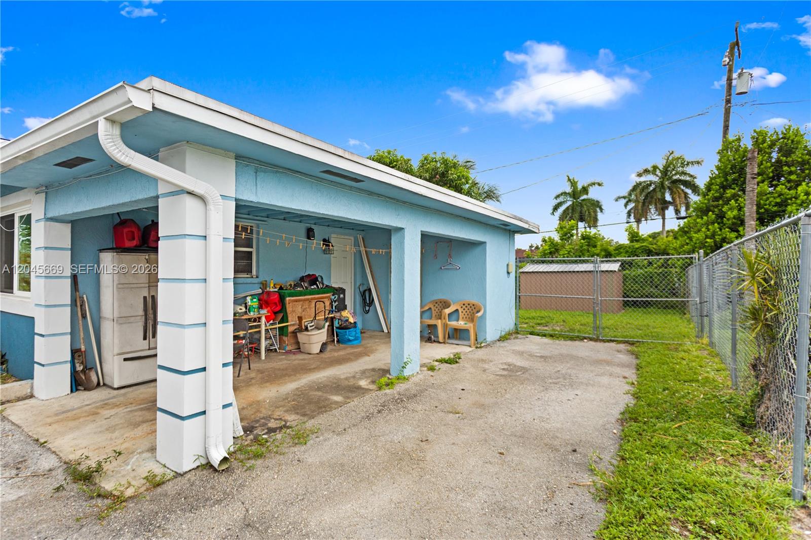 A light blue house features a covered carport with a concrete floor and chain-link fencing — 3030 NW 176th St, Miami Gardens FL 33056, MIAMI GARDENS, FL