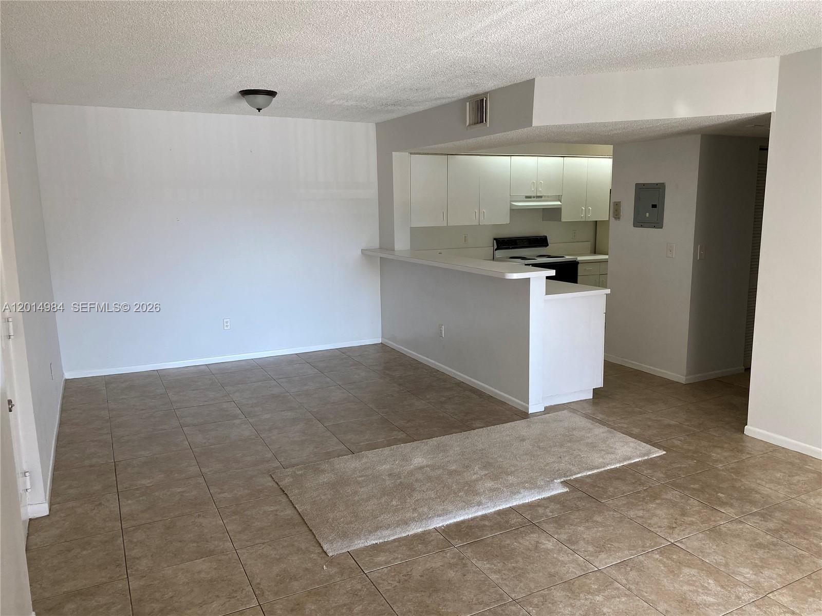 This room features beige tile flooring, a white breakfast bar, and an adjacent kitchen area — 18820 NW 57th Ave # 203, Hialeah FL 33015, HIALEAH, FL