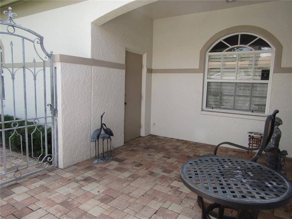 A paved patio features a metal gate, a window with shutters, and outdoor furniture — 3881 CHATSWORTH GREENE COURT UNIT 20, SARASOTA, FL