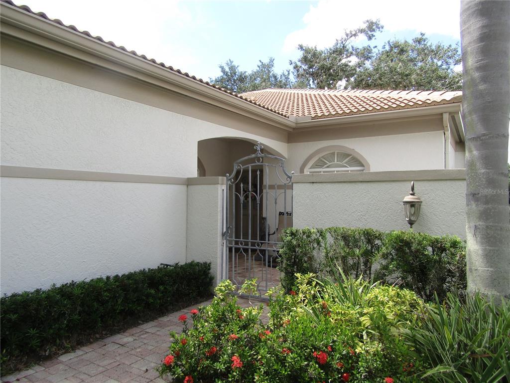 A brick walkway leads to a gated courtyard entrance of a stucco home with tile roofing — 3881 CHATSWORTH GREENE COURT UNIT 20, SARASOTA, FL