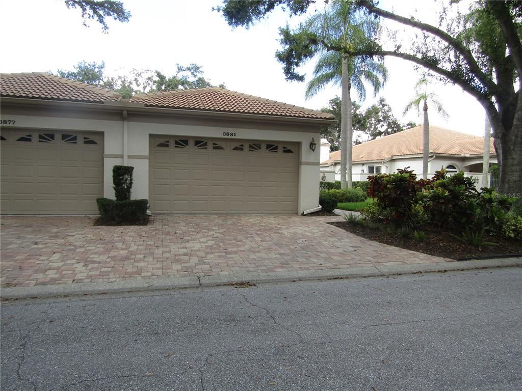 A beige house exterior features a two-car garage and a paved driveway — 3881 CHATSWORTH GREENE COURT UNIT 20, SARASOTA, FL