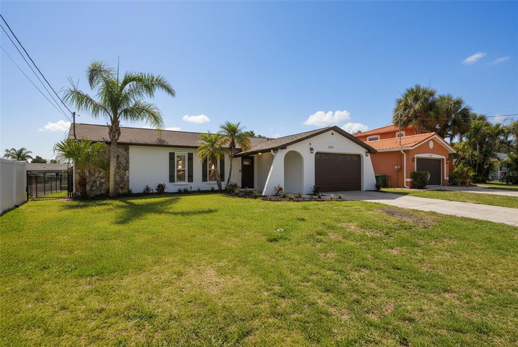 A single-story white house with a stone accent wall, palm trees, and a two-car garage — 13840 BARNARD AVENUE, HUDSON, FL