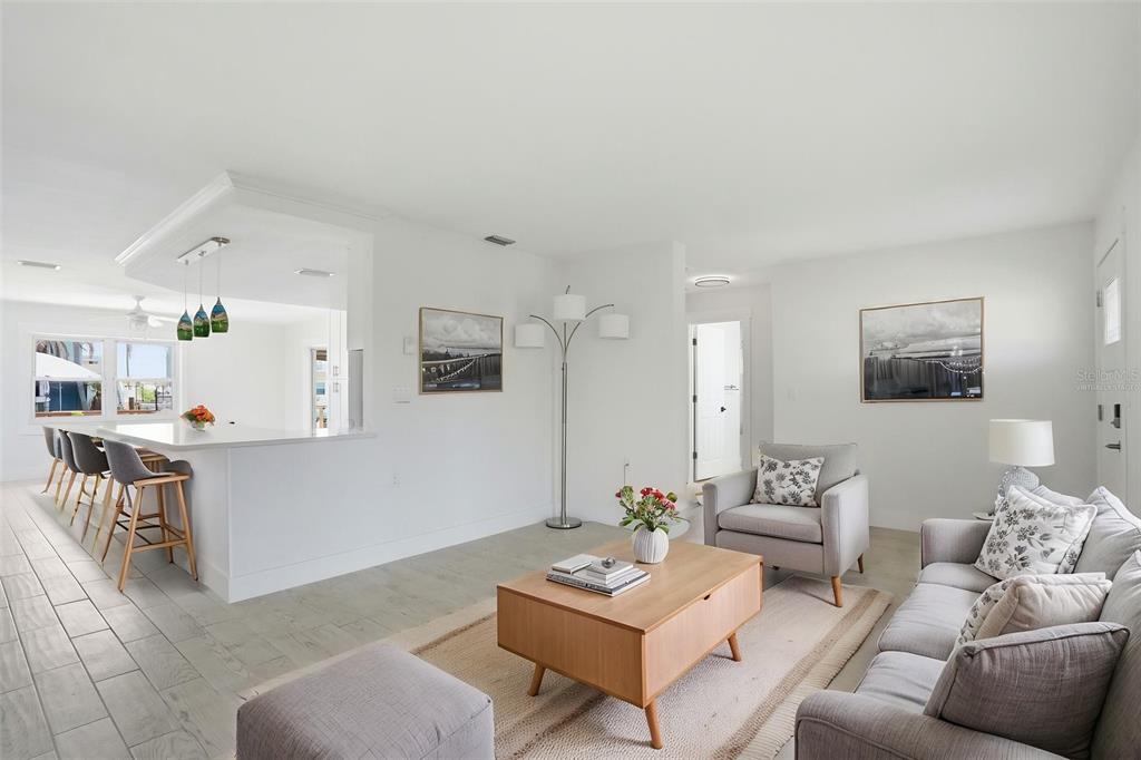 A bright living room features a kitchen island with bar stools, gray furniture, and artwork — 13840 BARNARD AVENUE, HUDSON, FL