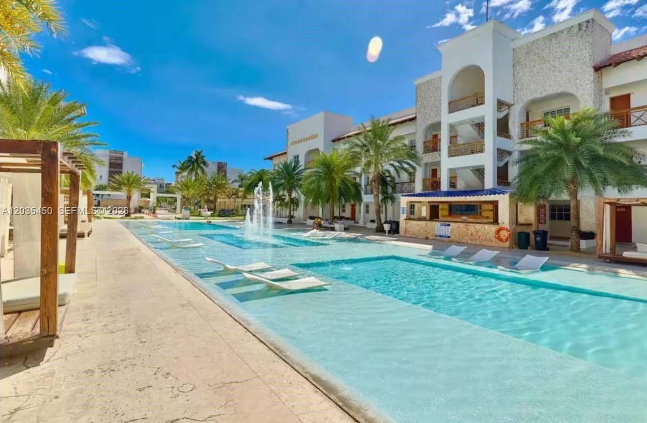 A large outdoor swimming pool with fountains and lounge chairs sits beside a multi-story building — 1 La Altagracia # 1, FL