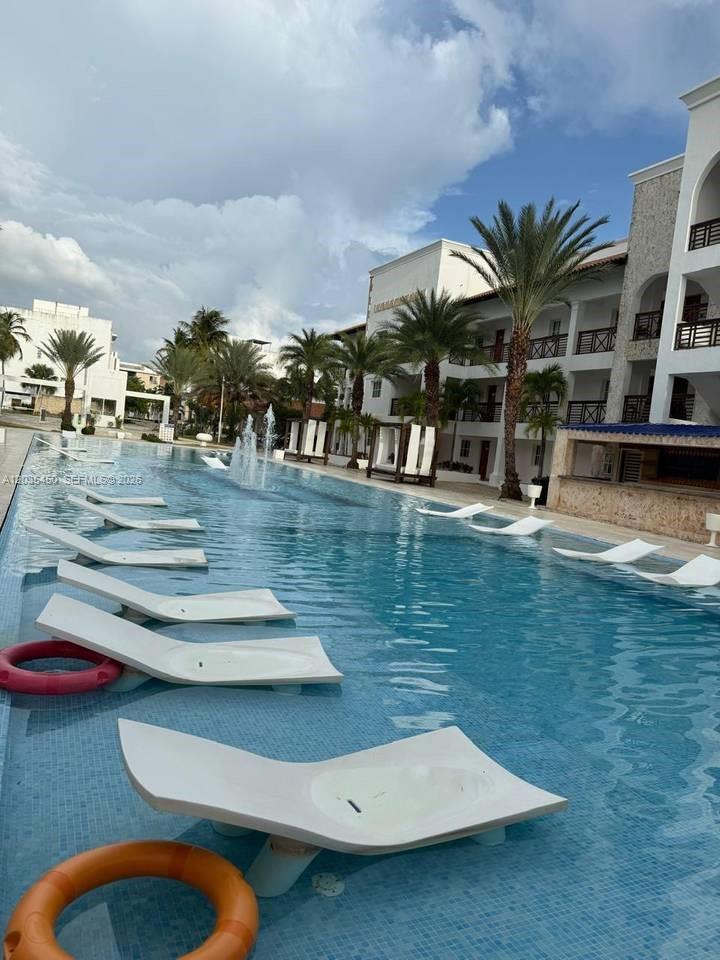 A long swimming pool features submerged lounge chairs and fountains beside a multi-story resort building — 1 La Altagracia # 1, FL