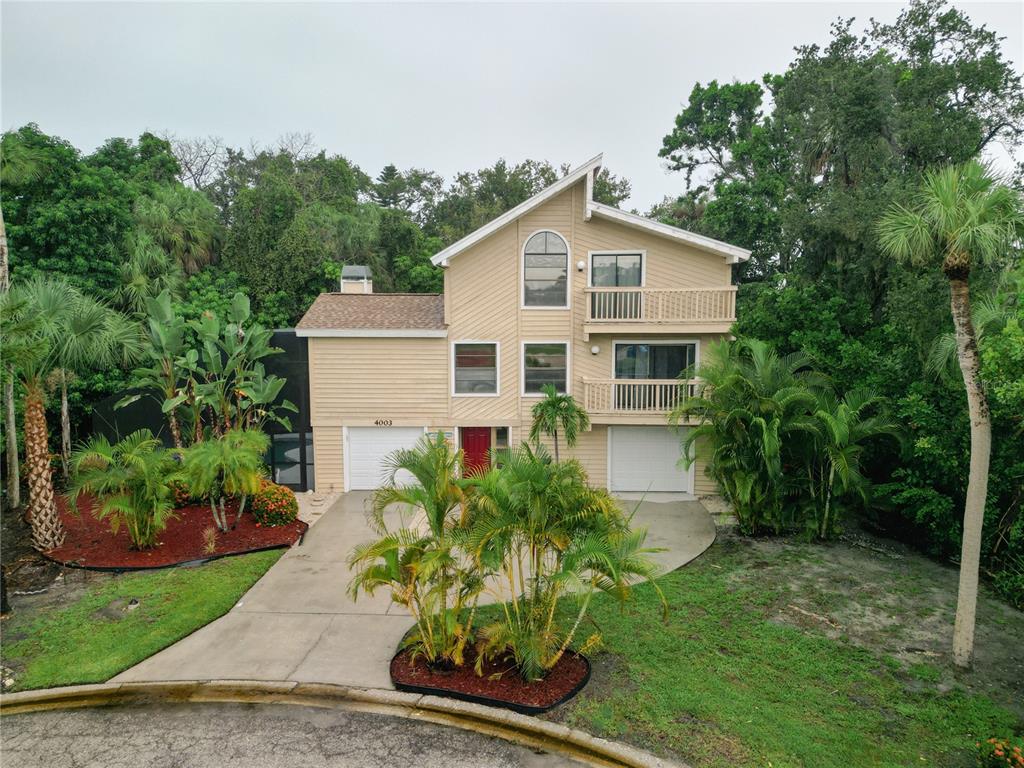 A two-story house with tan siding, two garage doors, and a balcony sits among trees — 4003 BAYSIDE COURT, BRADENTON, FL