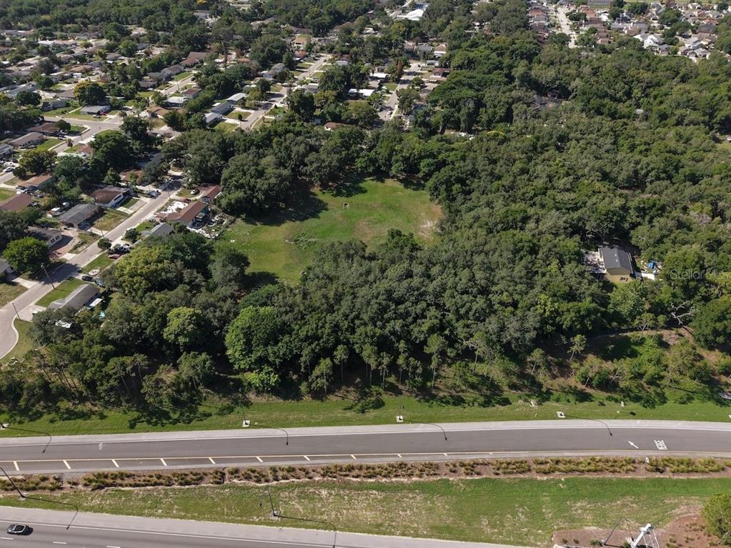 An aerial view shows a large, grassy vacant lot surrounded by trees and residential houses — 481 N LANCELOT AVENUE, ORLANDO, FL