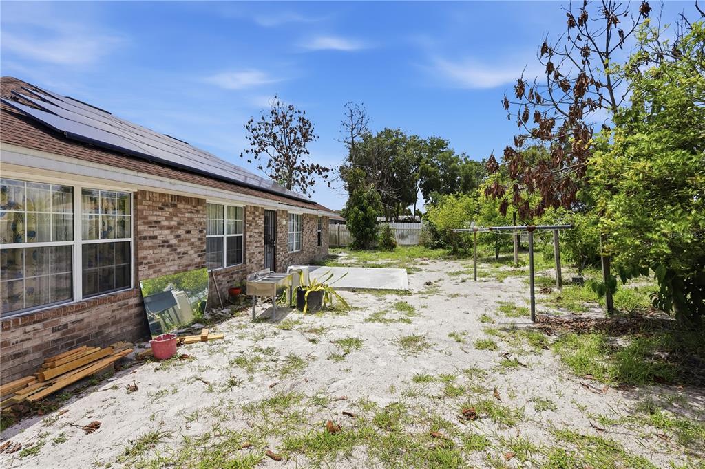 The exterior of a brick house features a sandy backyard with a concrete patio area — 964 FORT SMITH BOULEVARD, DELTONA, FL