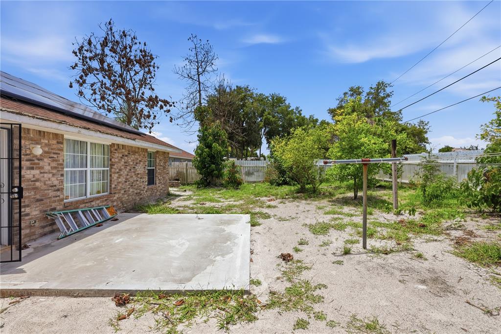 A brick house exterior features a concrete patio, a clothesline, and a sandy backyard — 964 FORT SMITH BOULEVARD, DELTONA, FL