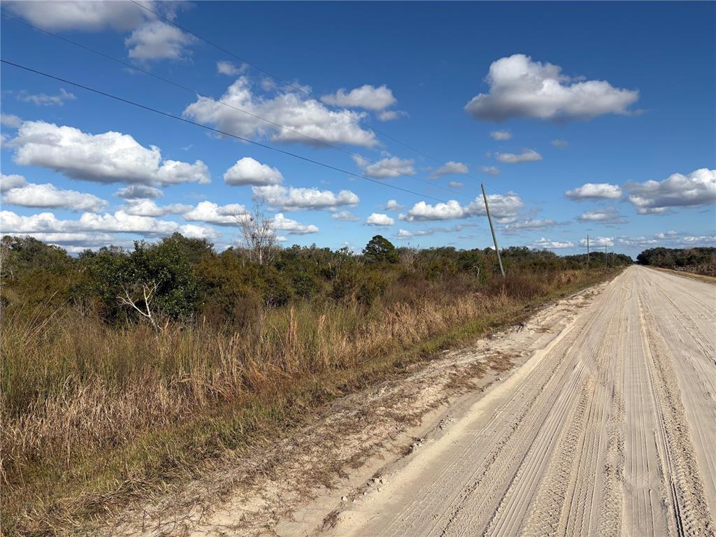 A dirt road runs alongside a plot of land with low-lying brush and trees — 22287 NW 264TH STREET, OKEECHOBEE, FL