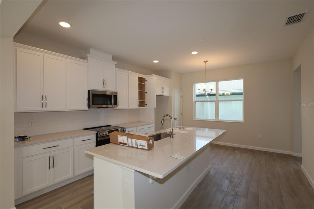 A kitchen with white cabinets, a quartz island, stainless steel appliances, and wood-look tile flooring — 1346 MOUNT ROYAL DRIVE, ST CLOUD, FL