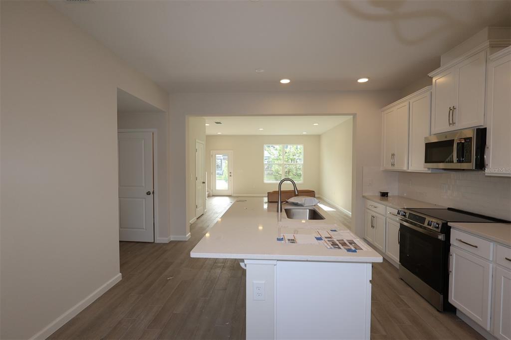 A modern kitchen with white cabinets, a large quartz island, and light wood-look flooring — 1346 MOUNT ROYAL DRIVE, ST CLOUD, FL