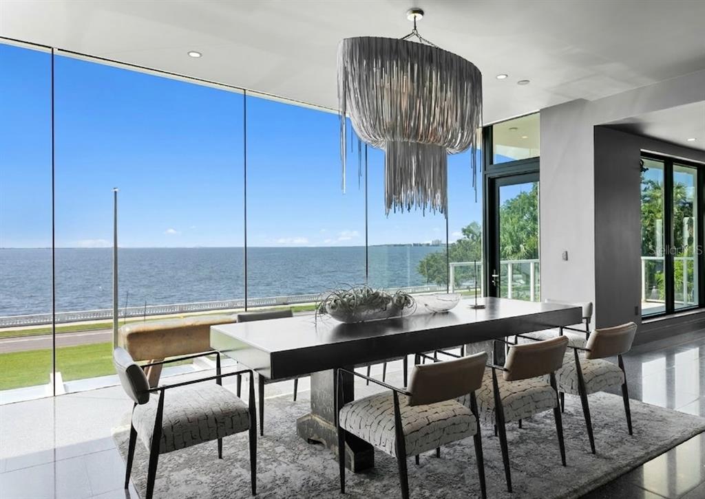 A modern dining room features a large table, a fringe chandelier, and floor-to-ceiling waterfront windows — 2619 BAYSHORE BOULEVARD UNIT 200, TAMPA, FL