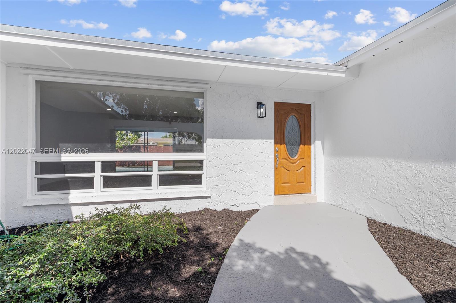 A white stucco house exterior features a large window, a wooden front door, and walkway — 7773 Coral Blvd, Miramar FL 33023, MIRAMAR, FL