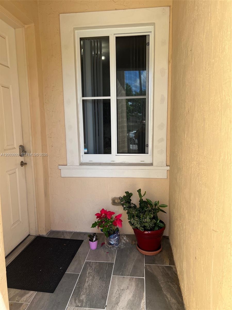 A tiled entryway features a white-framed window, a door, and several potted plants — 11021 SW 236th Ter, Homestead FL 33032, HOMESTEAD, FL
