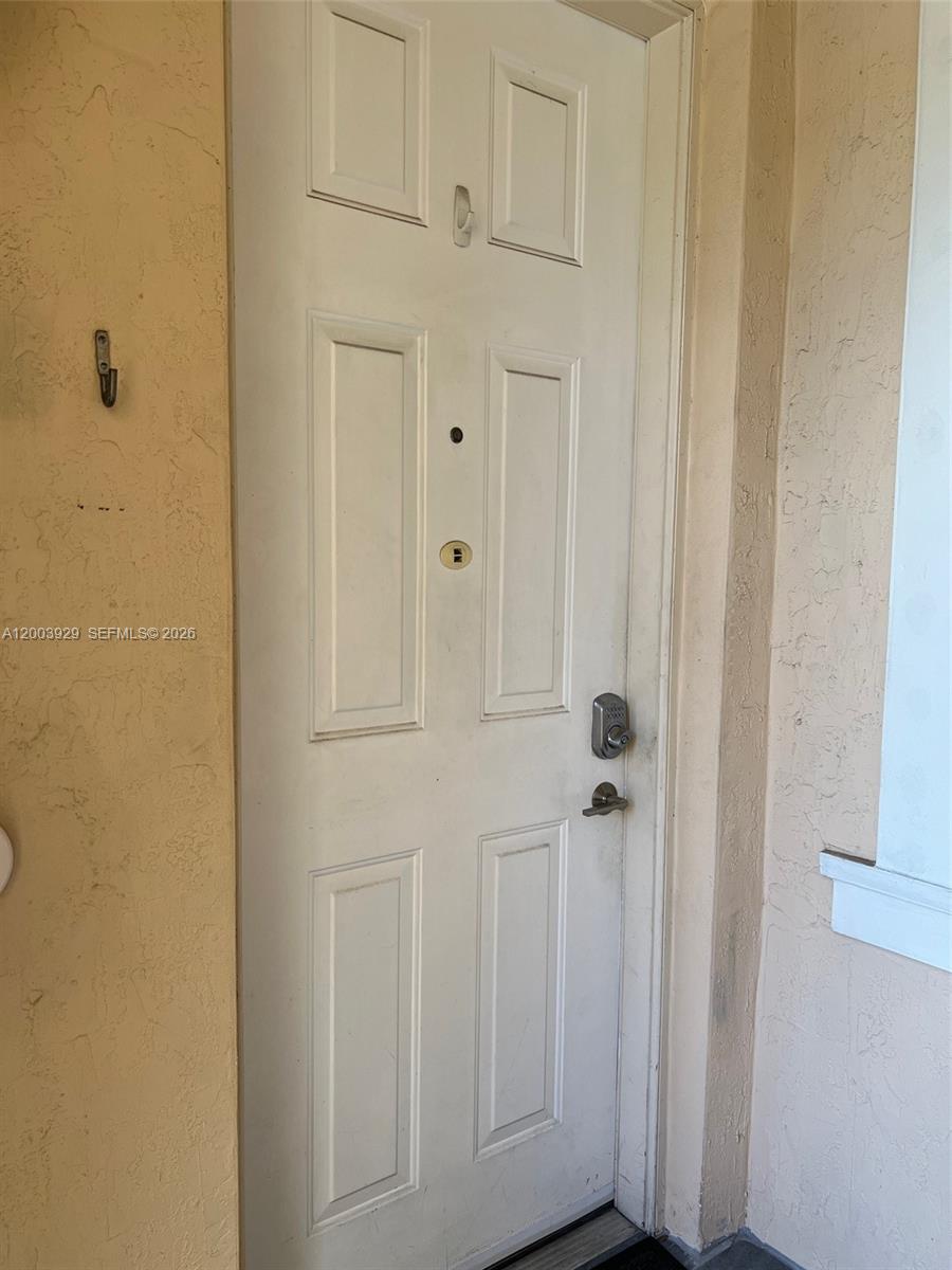 A white six-panel entry door with a smart lock is set in a stucco wall — 11021 SW 236th Ter, Homestead FL 33032, HOMESTEAD, FL