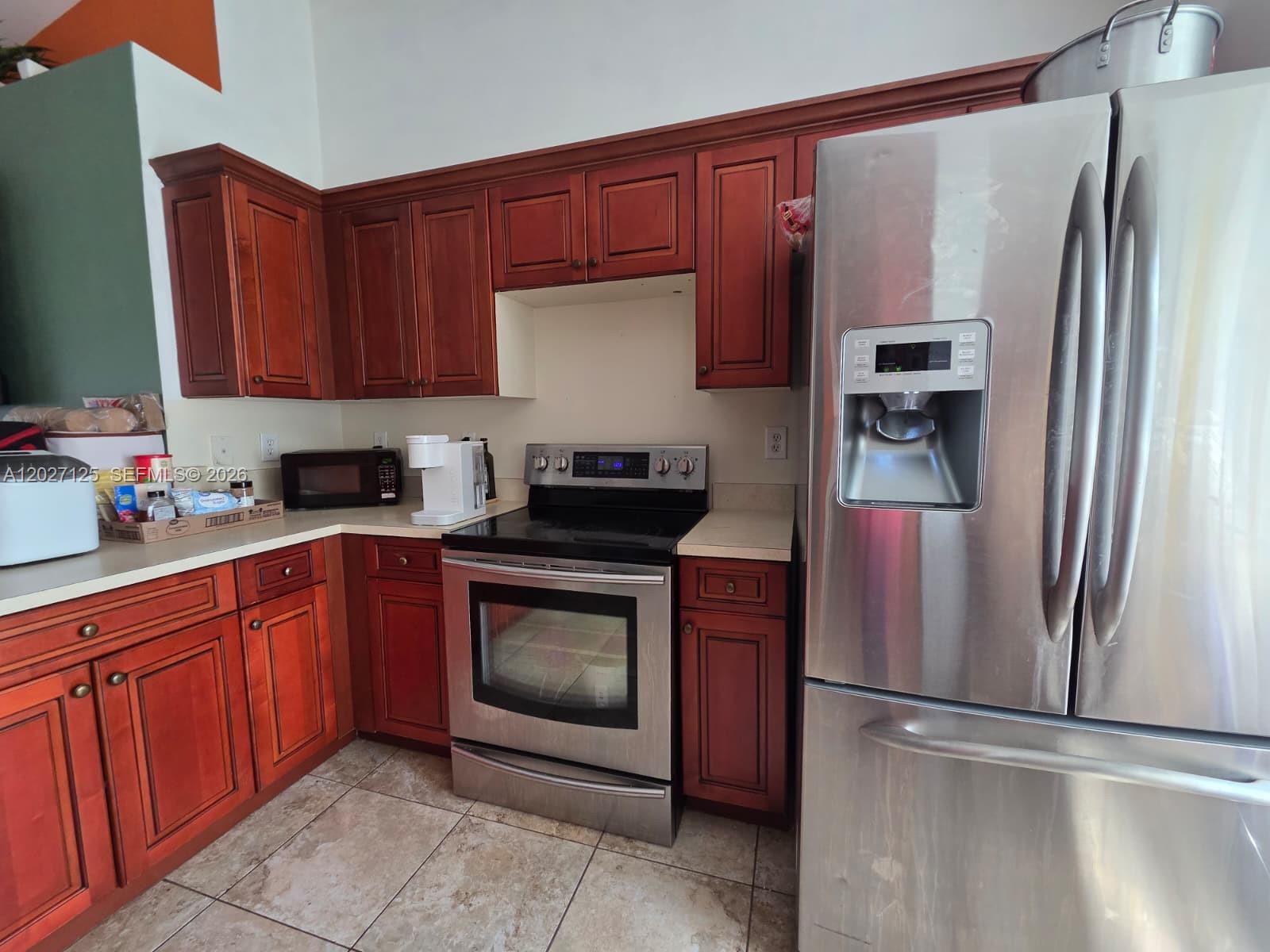 A kitchen features cherry wood cabinets, stainless steel appliances, and beige tile flooring — 3529 Sunshine BLVD, Lehigh Acres FL 33971, LEHIGH ACRES, FL