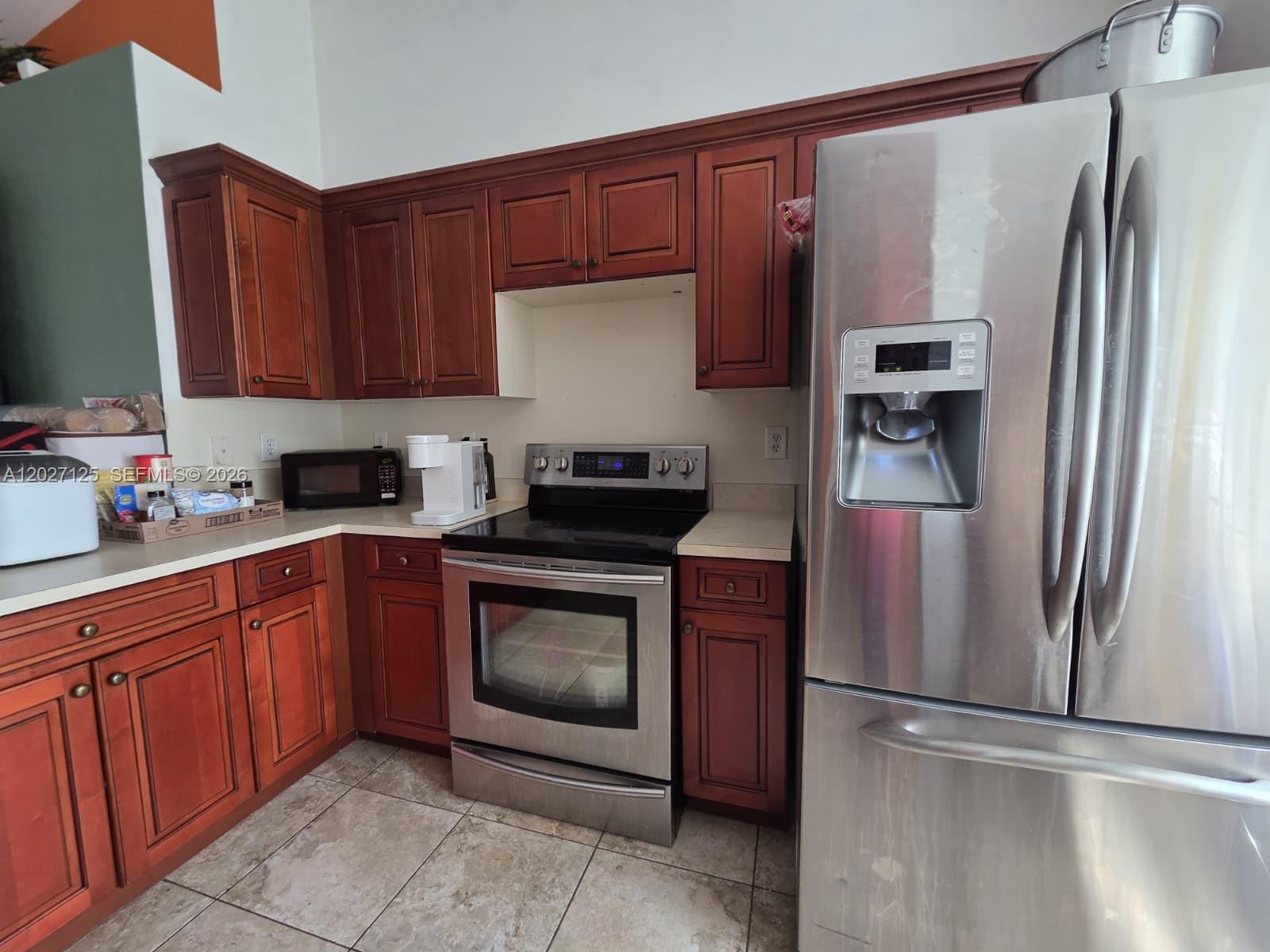 A kitchen features cherry wood cabinets, stainless steel appliances, and light-colored countertops — 3529 Sunshine BLVD, Lehigh Acres FL 33971, LEHIGH ACRES, FL