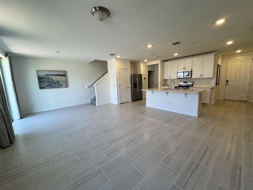 An open-concept kitchen and living area features light tile flooring, white cabinetry, and a peninsula — 4532 BURROWING OWL LOOP, ST CLOUD, FL