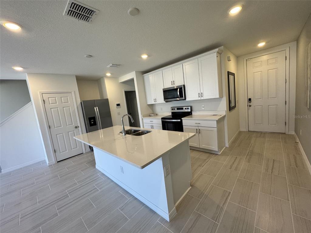 A modern kitchen features white cabinetry, stainless steel appliances, a quartz island, and tile flooring — 4532 BURROWING OWL LOOP, ST CLOUD, FL
