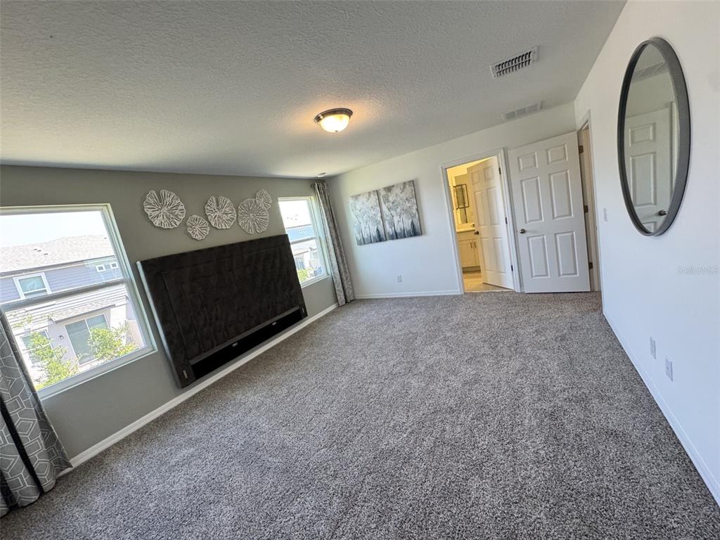 A carpeted bedroom features a dark headboard, wall art, a mirror, and an attached bathroom — 4532 BURROWING OWL LOOP, ST CLOUD, FL