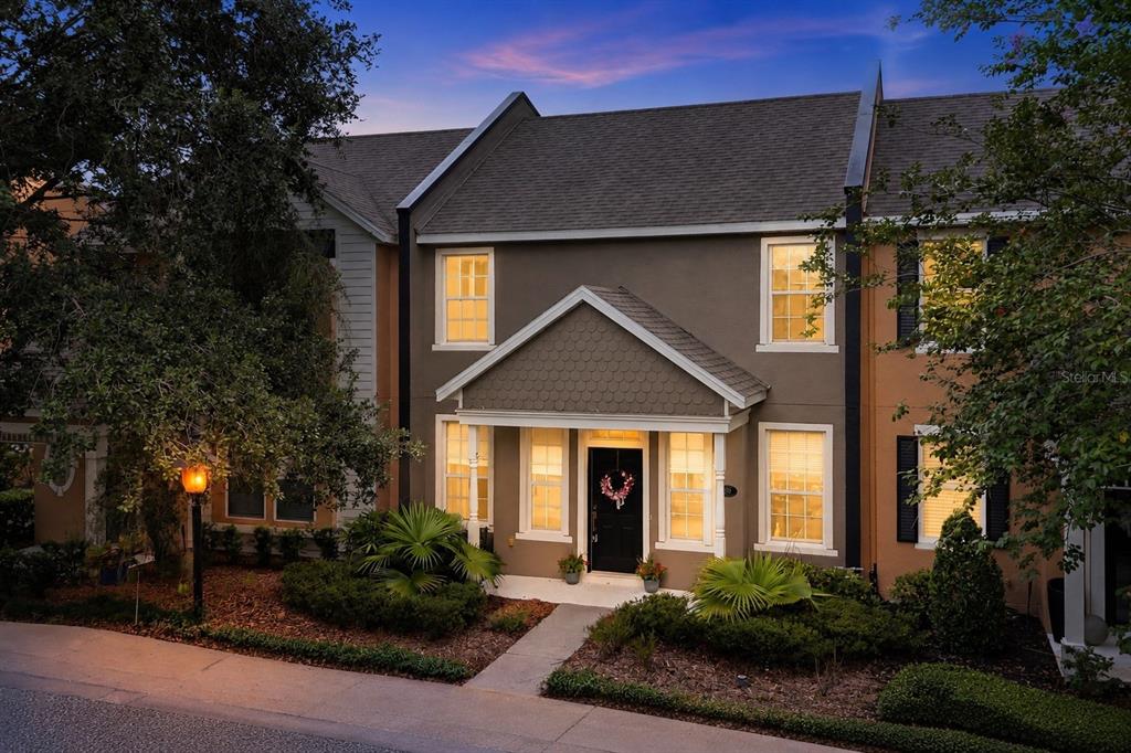 A two-story townhouse with a dark brown exterior, a gabled entryway, and illuminated windows — 809 WYNBROOK LANE, DELAND, FL