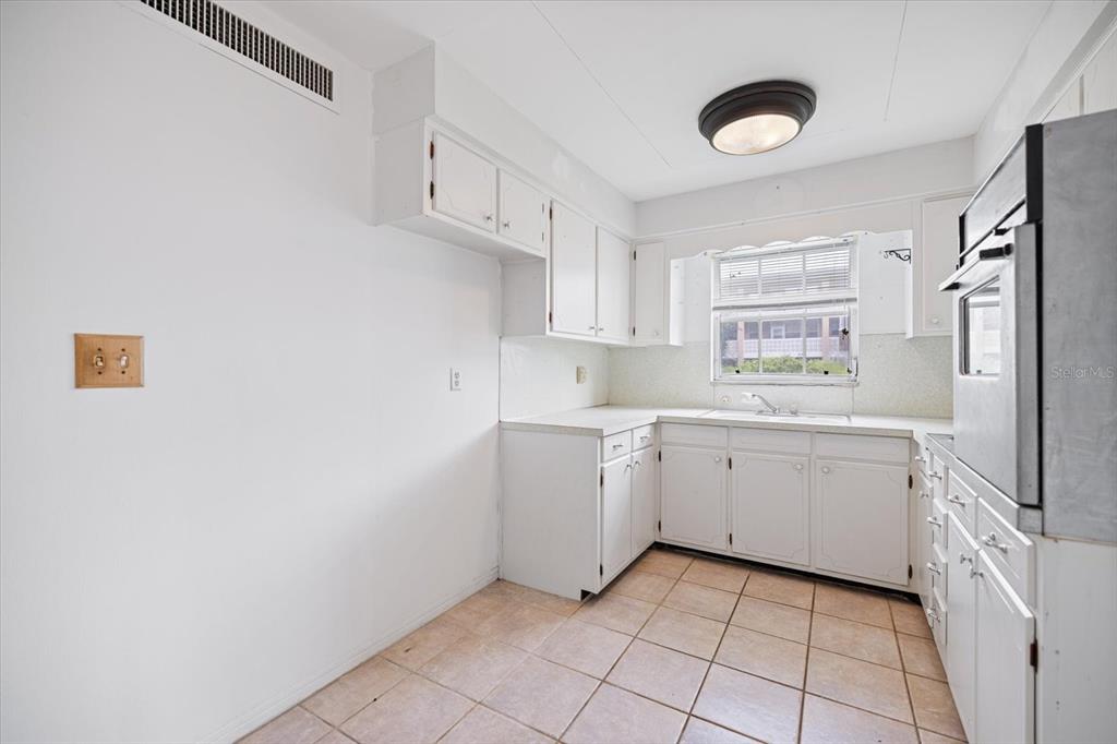 A kitchen with white cabinets, a wall oven, tiled floors, and a window above the sink — 450 32ND AVENUE N UNIT 106W, ST PETERSBURG, FL