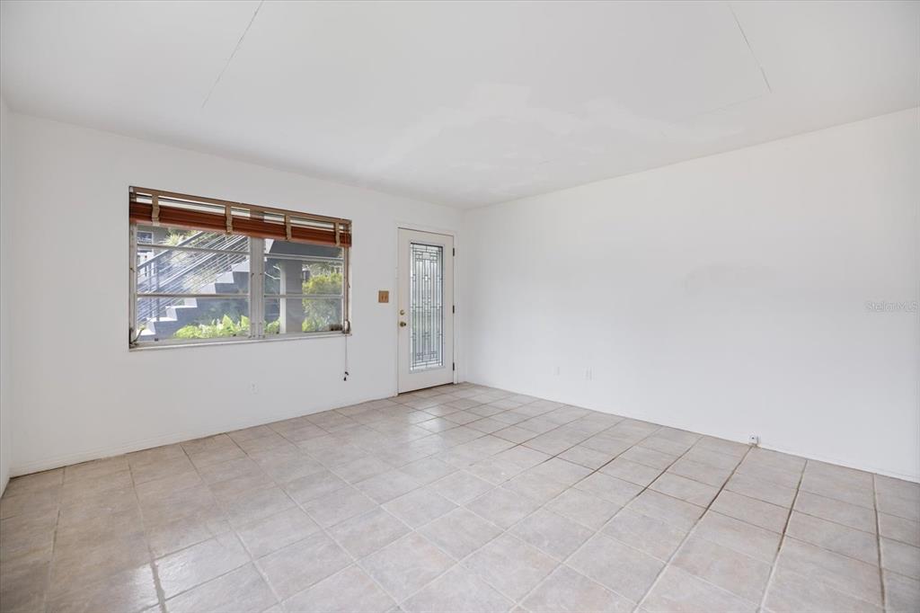An empty room with white walls, beige tile flooring, a window, and a glass-paneled door — 450 32ND AVENUE N UNIT 106W, ST PETERSBURG, FL
